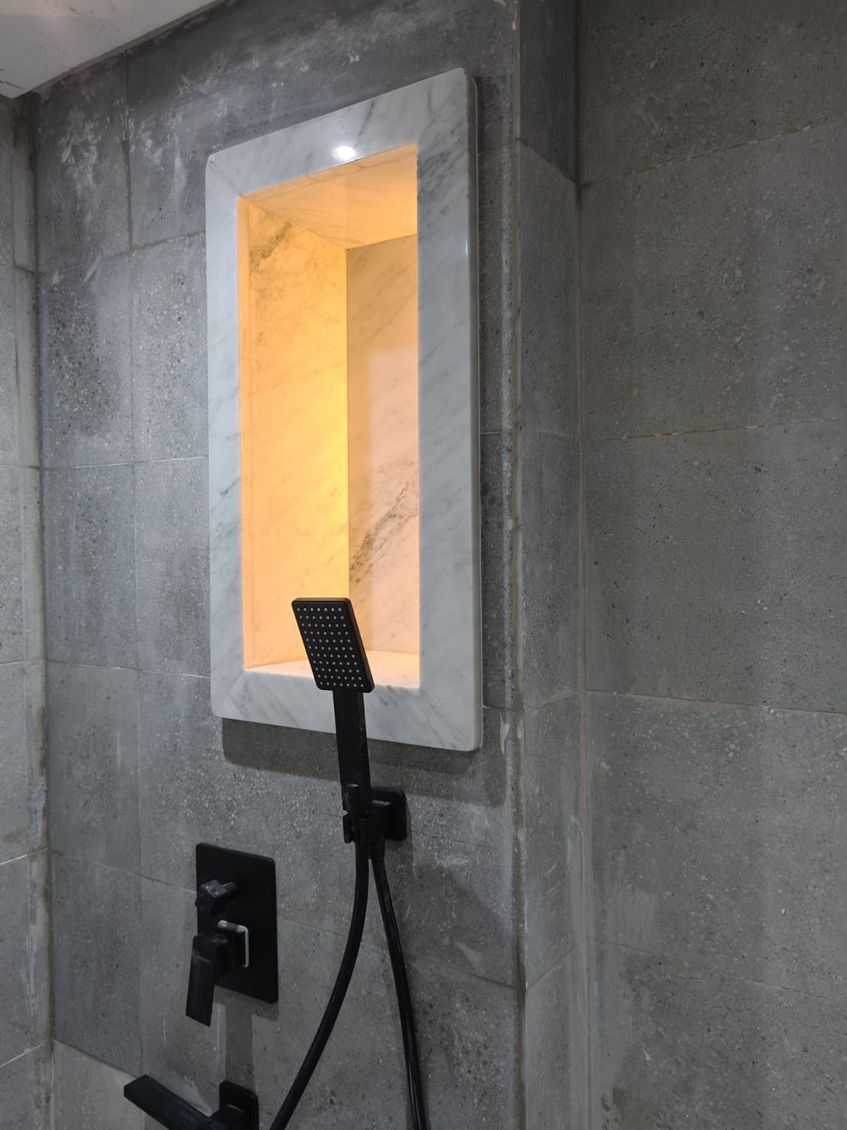Niche de douche en marbre blanc veiné, rétroéclairée, encastrée dans une paroi de pierre grise